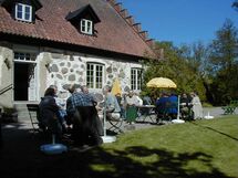 People sitting at tables outside a house. Photo.