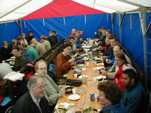 People having lunch along a long table. Photo.