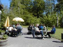 People sitting at tables outside a house. Photo.