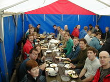 People having lunch along a long table. Photo.