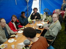 People having lunch along a long table. Photo.