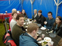 People having lunch along a long table. Photo.